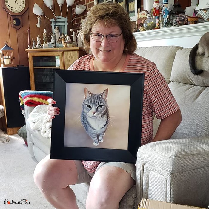 Picture of a woman holding cat portraits of her cat while sitting on couch