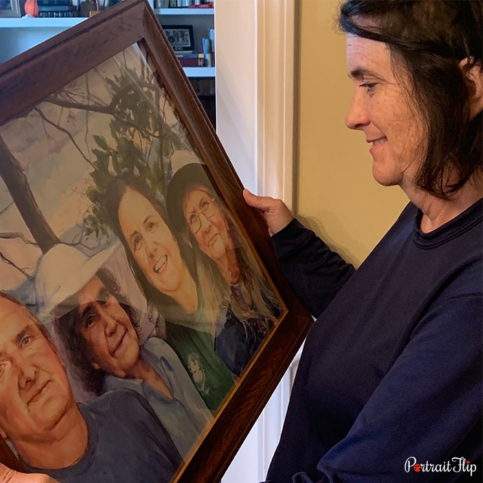 Picture of a woman holding mother’s day paintings while facing towards the portrait that includes three women and a man together